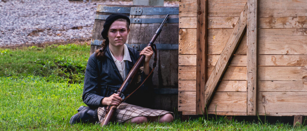 A powerful image of a female French Resistance soldier lying in the grass, poised and alert. Her expression shows determination as she surveys her surroundings, embodying the bravery and resilience of women in the fight against oppression during WWII.